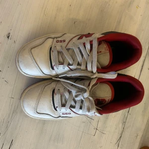 Vita och röda sneakers från New Balance - Snygga New Balance 550 sneakers i vitt med röda och svarta detaljer. Skorna har snörning och en sportig design som passar perfekt för en casual look. Perfekta för dig som gillar en stilren men ändå färgglad stil.