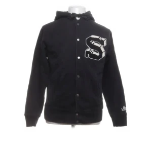 Svart hoodie från Stüssy - Säljer en svart hoodie från Stüssy med en stor bokstav 'S' på framsidan. Hoodien har långa ärmar och knappar framtill. Tillverkad i 100% bomull för en bekväm känsla. Perfekt för en avslappnad stil.