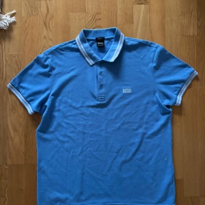 Blå pikétröja från Hugo Boss - Snygg blå pikétröja från Hugo Boss med vitrandig krage och knappslå. Perfekt för en stilren look. Regular fit för en bekväm passform.