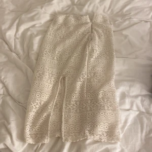 Vit spetskjol från H&M Divided - Säljer en elegant vit spetskjol från H&M Divided. Kjolen har en lång design med vackra spetsdetaljer och en subtil slits framtill. Perfekt för en stilren look.