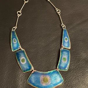 Vintage Unikt blått halsband med abstrakt design - Säljer ett unikt vintage halsband med stora blå emaljerade plattor i abstrakt design. Plattorna har en vacker blå färg med cirkulära mönster i grönt och vitt. Halsbandet är handgjort och signerat på baksidan.