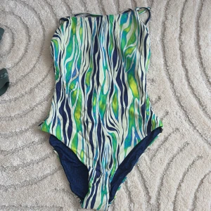 Mönstrad baddräkt från Arena - Snygg baddräkt från Arena med ett färgglatt mönster i blått, grönt och gult. Den har smala axelband och en öppen rygg med knytning. Perfekt för poolen eller en dag på stranden. Pris kan diskuteras.
