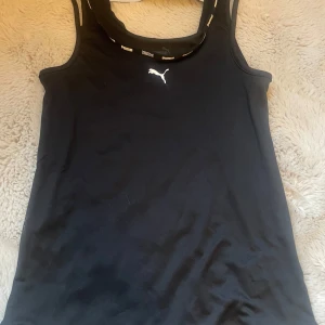 Svart linnetopp från Puma - Snygg svart linne från Puma med logga på bröstet och text på ryggen. Aldrig andvänd, köpt för 299kr