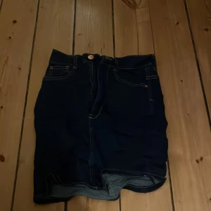 Mörkblå jeanskjol från Gina Tricot - Snygg mörkblå jeanskjol från Gina Tricot, modell Molly. Kjolen har en klassisk femficksdesign och stängs med knapp och dragkedja framtill. Perfekt för en avslappnad stil. Köpt på loppis för kanske 1år sen 