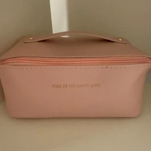 Rosa necessär från Rose of No Man's Land - Helt ny och snygg rosa necessär med dragkedja och praktiskt handtag. Perfekt för att organisera dina skönhetsprodukter. Den har en stilren design med guldiga detaljer som ger en lyxig känsla.