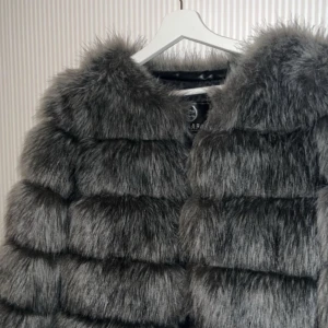 Grå pälsjacka - Säljer en supermjuk och fluffig grå pälsjacka. Perfekt för att hålla sig varm och stilren under kalla dagar. Jackan har en elegant design med långa ärmar och en bekväm passform. Perfekt för både vardag och fest!