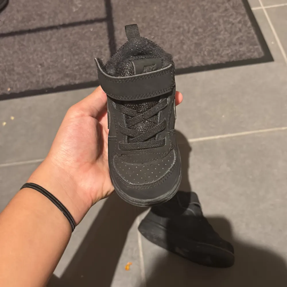 Säljer ett par svarta Nike sneakers för babysar mycket bra skick. Skorna har en stilren design med kardborreband och snörning för enkel på- och avtagning. Perfekta för både lek och vardag!. Skor.