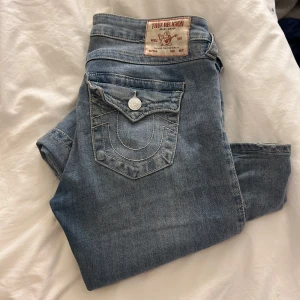 True Religion Joey Low Rise Flare Jeans - Säljer ett par snygga True Religion jeans i modellen Joey. De är lågmidjade med en flare-stil och kommer i en klassisk ljusblå denimfärg. Säljs pågrund av att jag inte får någon användning av de tyvärr, och därav använda fåtal gånger. Pendlar mellan s/m i byxor och dessa passar.🥰 (Pris kan diskuteras vid snabbt köp!)
