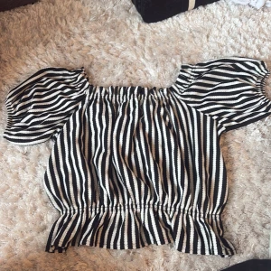 Randig offshoulder topp - Säljer en superfin randig offshoulder topp i svart och vit. Perfekt för sommardagar eller en avslappnad fest. Toppen är i  bra skick och redo för nya äventyr!