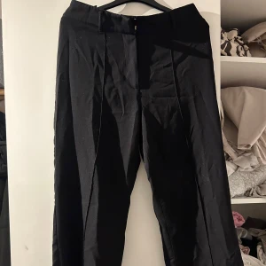 Svarta kostymbyxor - Snygga svarta kostymbyxor i klassisk stil. Perfekta för både kontoret och festliga tillfällen. De har en rak passform och är tillverkade i ett bekvämt material som ger en stilren look. Passar bra till en skjorta eller blus för en elegant outfit.
