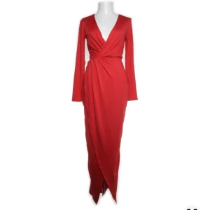 Röd långklänning från Nelly - Röd långklänning från Nelly, NLY EVE i storlek 36. Klänningen har en omlott-design med en elegant v-ringning och långa ärmar. Perfekt för festliga tillfällen med slits framtill. Materialet känns mjukt och bekvämt. Klänningen är bara använd en gång så i mycket bra skick!