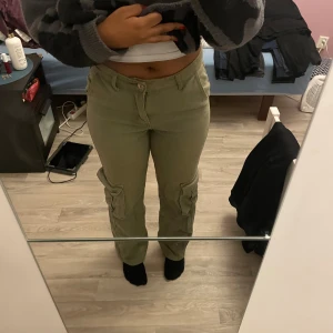 Olivgröna cargobyxor - Säljer ett par olivgröna cargobyxor i bra skick. De har en normal passform och är perfekta för höst och vår. Byxorna har praktiska fickor på sidorna och stängs med dragkedja och knapp. Perfekta för en avslappnad och stilren look!