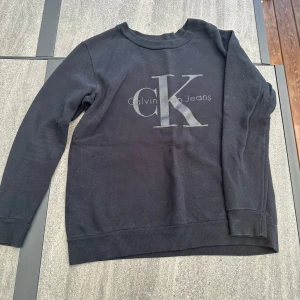Svart tröja från Calvin Klein Jeans - Säljer en svart tröja från Calvin Klein Jeans i bra skick. Den har en stor CK-logga på framsidan och är perfekt för både vardag och chill. 