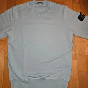 Ljusblå sweatshirt från Stone Island - Säljer en stilren ljusblå sweatshirt från Stone Island. Den är i nyskick.. Märkesloggan sitter snyggt på ärmen. Perfekt för en casual look!