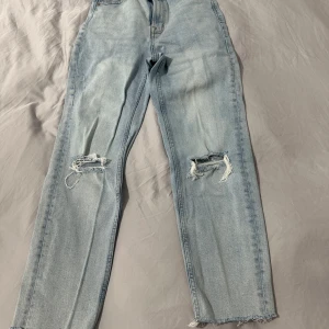 Stretchiga mom jeans med slitningar - Säljer ett par ljusa mom jeans i mycket bra skick. De har en straight passform och coola slitningar på knäna för en avslappnad look. Perfekta för vardagsbruk och ger en trendig touch till din outfit. Passar bra till både sneakers och boots!