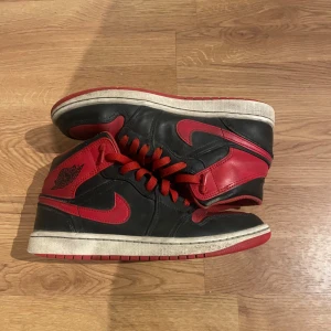 Nike Air Jordans i svart och rött - Säljer ett par klassiska Nike Air Jordans i svart och rött. Skorna har en snygg design med röd snörning och den ikoniska swoosh-loggan. De är i bra skick med lite slitage på sulan. Perfekta för både vardag och fest!