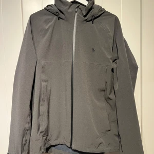 Grå vindjacka från Polo Ralph Lauren - Säljer en stilren grå vindjacka från Polo Ralph Lauren. Det är en sample jacka och den har packbar huva. Jackan är i mycket bra skick och nypris är 2500:-