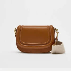 Zara väska - Snygg brun axelväska i skinn med justerbar axelrem i beige. Perfekt för både vardag och fest. Väskan har en stilren design med guldfärgade detaljer som ger en lyxig känsla. Passar till alla säsonger och är ett måste i garderoben!