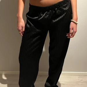 Svarta randiga byxor - Säljer ett par svarta byxor med diskreta ränder. De har en loose passform och är perfekta för både vardag. Materialet ser ut att vara mjukt och bekvämt, vilket gör dem idealiska för höst och vinter. Byxorna har en elastisk midja för extra komfort.