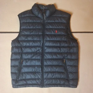 Ralph Lauren Mörkblå dunväst  - Säljer en snygg mörkblå dunväst från Ralph Lauren. Västen har en dragkedja framtill  med dragkedjor. Den är perfekt för höst och vår, och har en liten röd logga på bröstet. Väldigt stilren och lätt att matcha med andra kläder.