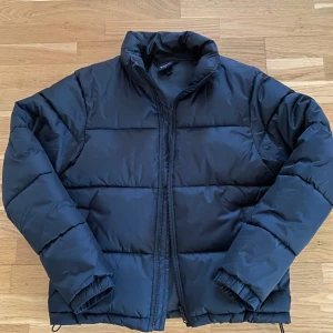 Svart pufferjacka från Everest - Säljer en svart pufferjacka från Everest i mycket bra skick. Jackan är perfekt för kalla dagar med sin tjocka vaddering och dragkedja framtill. Den har en klassisk design med långa ärmar och justerbar nederkant för extra komfort. Perfekt för både höst och vinter!