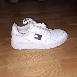 Säljer ett par vita sneakers från Tommy Jeans i mycket bra skick. Skorna har en klassisk design med snörning och det ikoniska Tommy Jeans-märket på sidan. Perfekta för både vardag och festliga tillfällen. De är bekväma och stilrena, ett måste i garderoben!