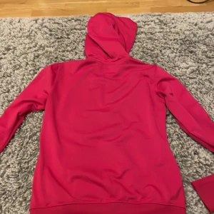 Röd huvtröja från Nike - Säljer en snygg röd huvtröja från Nike i storlek S. Den har en dragkedja framtill och en klassisk Nike-logga på bröstet. Perfekt för träning eller vardagsbruk. Huvan ger extra värme och stil. Passar perfekt till höst och vår!