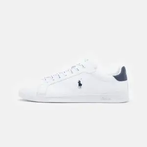 Säljer ett par vita sneakers från Polo Ralph Lauren med mörkblå detaljer och snörning. Skorna har en klassisk design med Polo-loggan på sidan och hälen. Perfekta för en avslappnad stil. Pris kan diskuteras med snabb affär