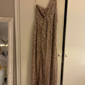  paljettklänning - En ursnygg paljettklänning med slit. Har en dragkedja på sidan och ett axelband. Passar perfekt till nyår, bröllop eller nu till balen om man vill ha något enklare. Storlek 34 men passar 36 utan problem då den är lite större i storleken. Glittar INTE av sig!!