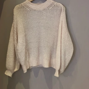Rosa stickad tröja - Mysig beige stickad tröja med en luftig design. Perfekt för kyliga dagar med sin bekväma passform och ribbade detaljer vid ärmslut och nederkant. Passar både till vardags och mysiga hemmakvällar.