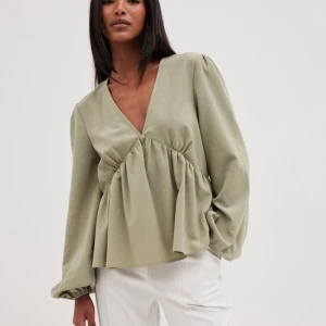 Grön blus - Säljer en superfin olivgrön blus med v-ringning och långa ärmar från nakd som är slutsåld. Blusen har en lös passform med en snygg rynkad detalj under bysten som ger en fin siluett. Perfekt för både vardag och fest! Endast använd en gång 