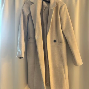 Beige kappa från Vero Moda - Säljer en stilren beige kappa från Vero Moda i storlek XS. Den har  två knappar framtill och långa ärmar. Perfekt för höst och vår, . Kappan är i mycket bra skick och redo för nya äventyr!