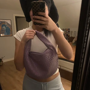 Lila flätad axelväska - Säljer en superfin lila axelväska i flätat mönster. Perfekt för att ge din outfit en färgklick! Väskan har en praktisk dragkedja och är i mycket bra skick. Den är både snygg och funktionell, perfekt för vardagsbruk eller en utekväll. 👜💜