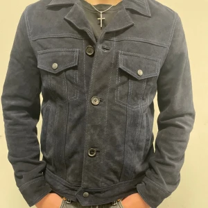 Mörkblå mockajacka från Zadig & Voltaire - Säljer en snygg mörkblå mockajacka från Zadig & Voltaire. Jackan har en klassisk design med knappar framtill och två bröstfickor med lock. Jackan är i nytt skick och går för cirka 6000 kr ny. Modellen på bilden är 180 cm lång.