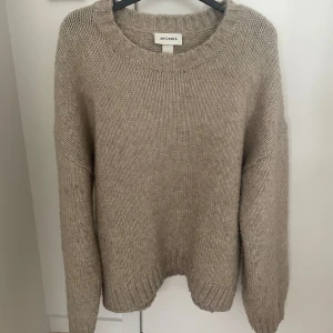 Beige stickad tröja från Monki - Säljer en supermysig beige stickad tröja från Monki. Perfekt för kyliga dagar med sin lösa passform och långa ärmar. Den har en klassisk rund hals och ribbade kanter som ger en stilren look. Passar perfekt till både jeans och kjol. 🧶✨
