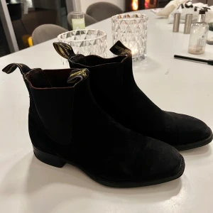 Svarta RM Williams boots i mocka 38 - Mycket fina svarta RM Williams boots i svart mocka , storlek 38 med dragflikar för enkel påtagning. Perfekta för en stilren look. Skorna är handgjorda i Australien och kostar mellan 5000-6000 kr nya. Bootsen är i fint skick. Skorna har varit hos skomakare och fått en tunn gummisula på lädersulan för att bättre stå emot regn och rusk. 1 mycket bra pris för dessa fina bords.