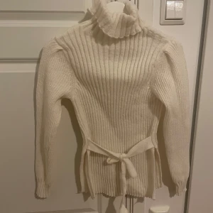 Vit ribbad polotröja med knytband - Snygg vit ribbad polotröja med långa ärmar och ett knytband i midjan. Perfekt för kyligare dagar med sin höga krage och stilrena design. Denna tröja är från SHEIN och är använd fåtal gånger. För fler frågor och bilder kan man kontakta mig privat🤍
