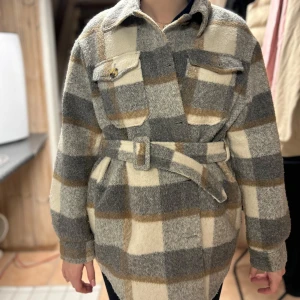 Rutig jacka  med bälte - Säljer en snygg rutig jacka i beige, grå och brun med bälte i midjan. Jackan har långa ärmar och knappar framtill samt två bröstfickor med lock. Perfekt för höst och vår! Jackan är köpt på vero Moda✨✨🤩