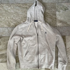Ralph Lauren - Zip Hoodie Grå Tröja Zip-Up Mjuk - S / Small - Ralph Lauren zip i grå, storlek S. Mjuk inuti, lite mjukis/ pyjamas-känsla. Vita snören. En modell som inte säljs längre (nya är grå inuti och annat material). Finns QR-kod som tar en till RLs hemsida och bekräftar äktheten 