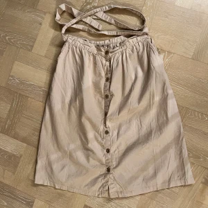 Beige kjol med knappar 100% lin  - Somrig och fin kjol med knappar framtill och ett knytband i midjan. 100% linne