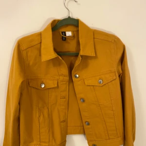 Senapsgul jeansjacka från H&M Divided - Snygg senapsgul jeansjacka från H&M Divided i storlek XS. Jackan har en klassisk design med knappar framtill och två bröstfickor med knappstängning. Perfekt för vår och sommar därför bra att köpa redan nu!🤍✨