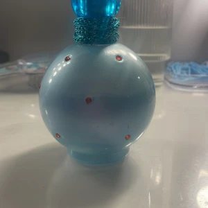 Blå parfymflaska med röda stenar - Säljer en elegant blå parfymflaska från Britney Spears, dekorerad med små röda stenar. Flaskan rymmer 100 ml och har en rund form med en matchande blå kork. Perfekt för den som älskar en stilren och glittrande design,nu skulle jag gissa att det är 60-70 ml i flaskan,köpte för 250