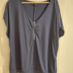  topp med dragkedja - Snygg blå topp med v-ringning och dragkedja framtill. Perfekt för en avslappnad stil. Bra skick, dock lite nopprig. Är typ storlek XL