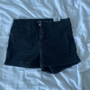 Låg midjade Svarta shorts från Jacqueline de Yong - Snygga lågmidjade svarta shorts från Jacqueline de Yong med upprullade benslut och knappdetalj. Perfekta för en avslappnad stil.