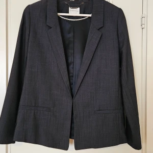 Mörkblå kavaj från Stockh LM - Snygg mörkblå lyxig kavaj från Stockh LM i storlek 38, med fina detaljer. Kavajen har en klassisk design med långa ärmar och två fickor framtill och med en diskret hake istället för knappar. Den är köpt för flera tusen kr men har hängt oanvänd i garderoben då den är för liten för mig. Den är liten i storleken, snarare 36 än 38, och vill man ha en oversized look bör man vara lite mindre storleksmässigt. 
