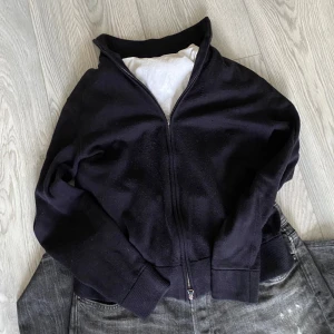 Svart merinoulltröja från These Glory Days - Säljer en stilren svart tröja i merinoull från These Glory Days. Tröjan har en dragkedja framtill och långa ärmar, perfekt för kyligare dagar. Den är mjuk och bekväm med ribbade muddar vid ärmslut och nederkant.