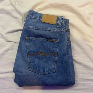 Blå jeans från Nudie Jeans - Snygga blå jeans från Nudie Jeans med klassisk femficksdesign och en bekväm passform. De har en subtil broderad detalj på bakfickan och en midwaist skärning. Perfekta för en avslappnad stil.