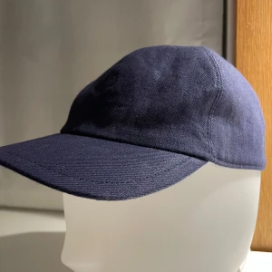 Mörkblå keps från Loro Piana - Snygg mörkblå keps från Loro Piana med broderad logotyp framtill. Kepsen är tillverkad i Italien och har en justerbar rem baktill för perfekt passform. Perfekt för en stilren look.