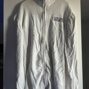 Vit tröja med dragkedja från HZR-ON - Säljer en vit tröja med dragkedja från HZR-ON. Tröjan har en ribbad struktur upptill och långa ärmar. Perfekt för kyligare dagar.