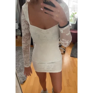 Vit student klänning - Elegant vit klänning med blommigt mönster och långa mest ärmar. Den har en tight passform och en öppen rygg med knytning. Perfekt för student eller midsommar. Aldrig använd, prislapp kvar. Ordinariepris 1500kr💞